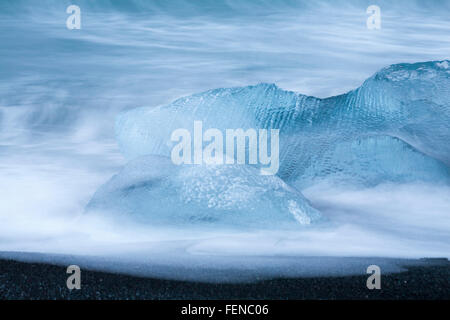Lange Belichtung der Wellen über eisblöcke kontrastieren mit schwarzem Sand am Gletschersee Jökulsárlón glazialen Strand, Diamond Beach, Island im Januar Stockfoto