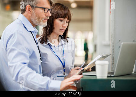 Geschäftsleute mit Zwischenablage funktioniert am Laptop in Fabrik Stockfoto