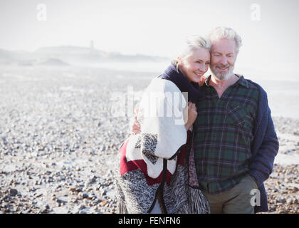 Lächelnde älteres paar zu Fuß am Strand Stockfoto