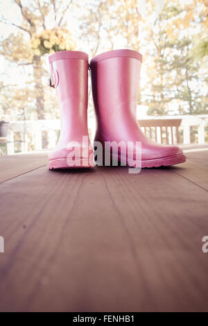 Ein paar rosa Gummistiefel oder "Wellies" sitzt auf einer Holzfläche im Herbst. Stockfoto
