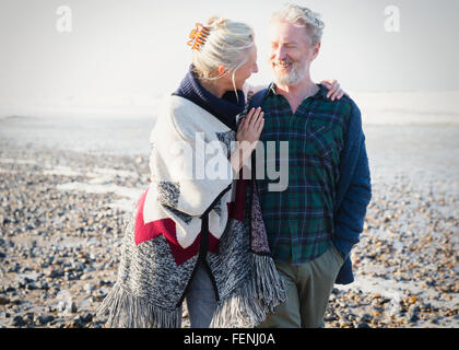 Älteres Paar zu umarmen und zu Fuß auf sonnigen felsigen Strand Stockfoto