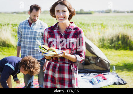 Porträt, lächelnde Frau mit Gegrillte Hamburger auf sonniger Campingplatz Stockfoto