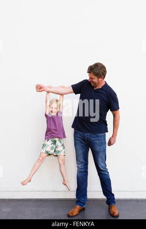 Porträt von reifer Mann mit Tochter von seinen Arm vor weißer Wand hängen Stockfoto