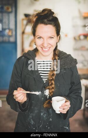 Porträt der jungen Frau mit Tontopf und Pinsel, Blick auf die Kamera zu Lächeln Stockfoto