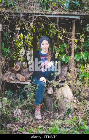 Junge Frau trägt Strick Hut sitzt bei der Brennholz Lagerung Schuppen wegschauen Stockfoto