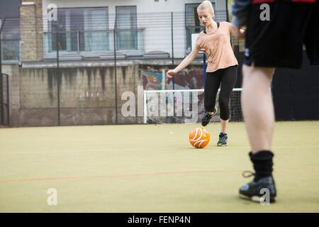 Junge Frau, die Fußball spielen auf städtischen Fußballfeld Stockfoto