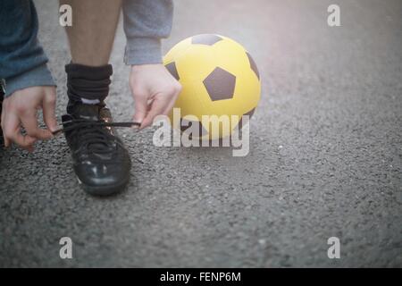 Junger Mann binden Schnürsenkel, Fußball neben ihm, niedrige Abschnitt Stockfoto