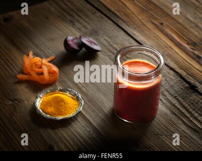 Erhöhte Ansicht roh Orangensaft in ein Glas mit Roter Beete, Kurkuma und geriebene Karotten auf Holzmaserung Muster Hintergrund Stockfoto