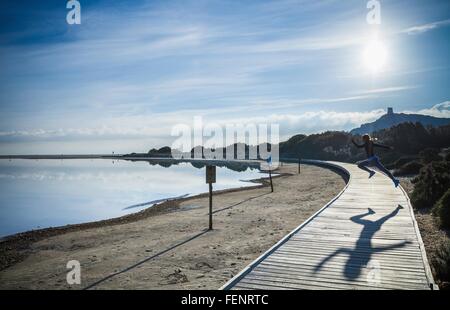 Junge Frau springen Luft über Beach Boardwalk, Villasimius, Sardinien, Italien Stockfoto