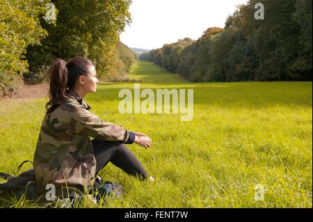 Junge Frau sitzt im Feld Blick auf Landschaft, Great Missenden, Buckinghamshire, Großbritannien Stockfoto