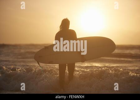 Silhouette des jungen männlichen Surfer mit Surfbrett im Meer, Devon, England, UK Stockfoto