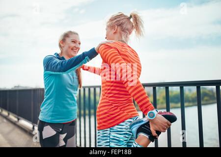 Zwei weibliche Läufer tun Aufwärmübung zusammen am Steg Stockfoto