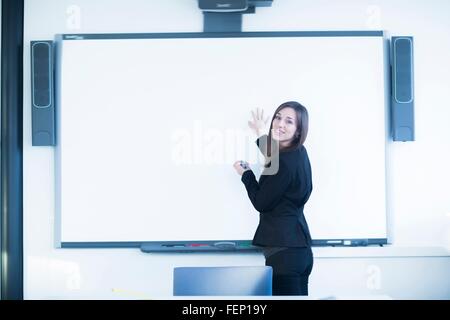 Junge Frau im Büro mit Whiteboard, Blick über die Schulter in die Kamera Lächeln Stockfoto