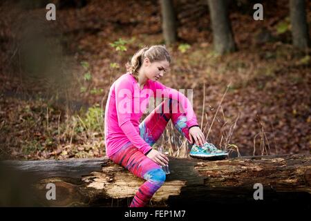 Seitenansicht der junge Frau trägt Sportkleidung auf umgestürzten Baum nach unten sitzen Stockfoto