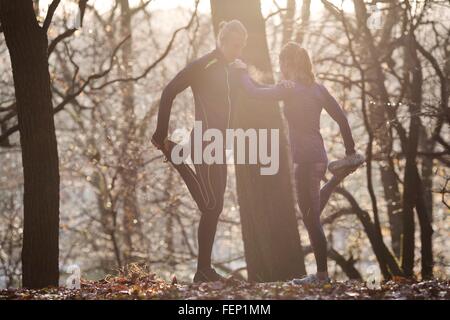 Paar im Wald lehnt sich an jedem anderen Bein angehoben Betrieb Fuß dehnen Stockfoto