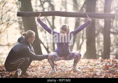 Junge Frau im Wald hocken Arme angehoben halten Ast Stockfoto