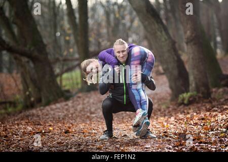 Mitte erwachsener Mann kauert im Wald tragen junge Frau auf Schultern, Blick auf die Kamera zu Lächeln Stockfoto