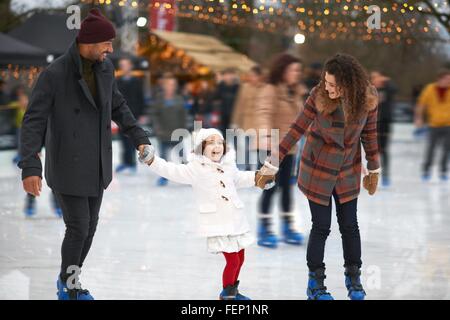 Mädchen halten Eltern Hände Eis Schlittschuhlaufen, Lächeln Stockfoto