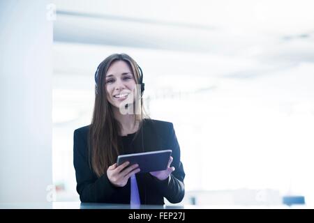 Junge Frau trägt Telefon Kopfhörer halten digital-Tablette Blick auf die Kamera zu Lächeln Stockfoto