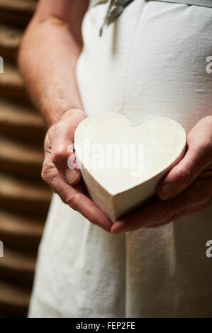 Sicht der Person trägt Schürze hält herzförmige Geschenkbox beschnitten Stockfoto