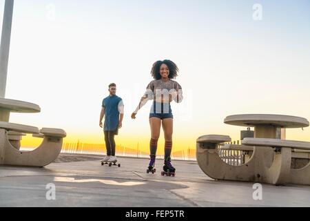 Junger Mann mit Skateboard, nach Mitte Erwachsene Frau auf Skates Stockfoto