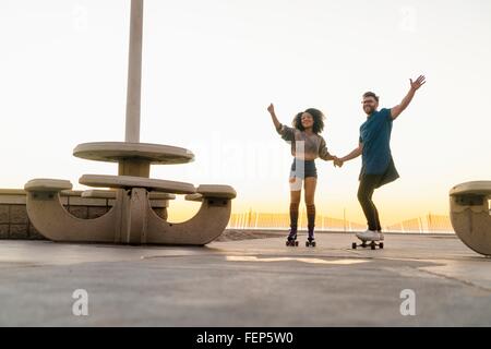 Paar mit Skates und Skateboard, Hand in Hand, Lächeln Stockfoto