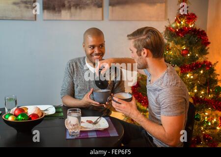 Männliche paar sitzt am Tisch, frühstücken gemeinsam, Weihnachtsbaum im Hintergrund Stockfoto