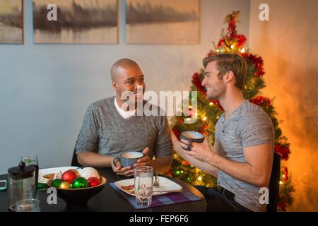 Männliche paar sitzt am Tisch, frühstücken gemeinsam, Weihnachtsbaum im Hintergrund Stockfoto
