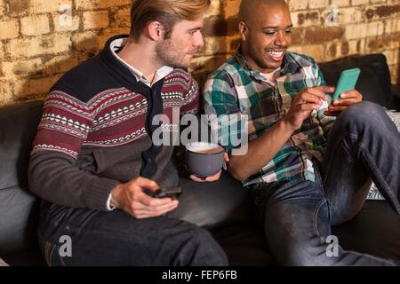 Männlichen Partner auf Sofa, Blick auf smartphones Stockfoto