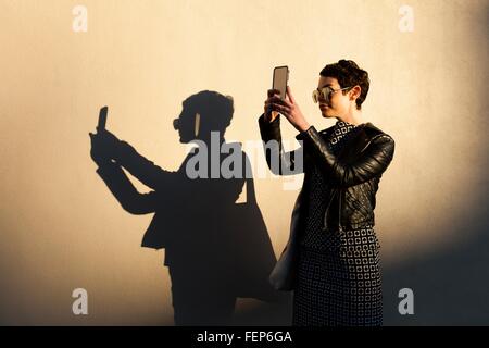 Mitte Erwachsene Frau unter Selbstbildnis, mit Smartphone shadow Cast an Wand neben ihr Stockfoto