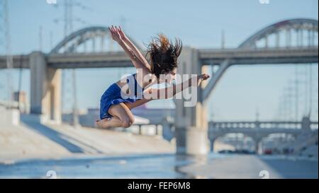 Seitenansicht der Tänzer springen in der Luft vor Brücke, Los Angeles, Kalifornien, USA Stockfoto