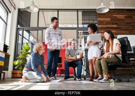 Gruppe von kreativen Menschen diskutieren neues Projekt. Frau sitzt mit dokumentiert locker am Boden und während einer Sitzung mit Lächeln ich Stockfoto