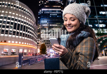 Frau im Wintermantel mit Smartphone in der nächtlichen Stadt Stockfoto