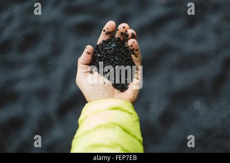 Hand der Mitte erwachsenen Mann mit schwarzem Sand, Draufsicht, Island Stockfoto