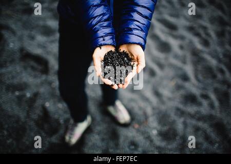 Händen der Mitte Erwachsene Frau mit schwarzer Sand, obenliegende Ansicht, Island Stockfoto