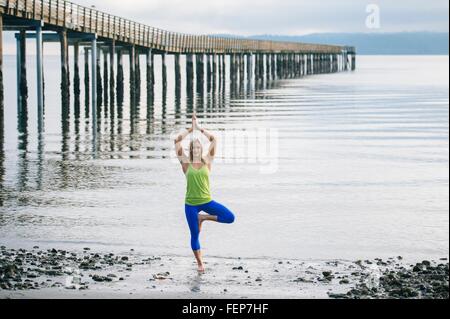 Porträt der jungen Frau praktizieren Yoga stehen Baumpose am Strand Stockfoto