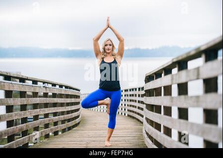 Porträt der jungen Frau üben stehenden Baum-Yoga-Pose auf hölzerne pier Stockfoto