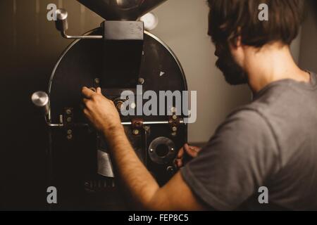 Man gießt Kaffeebohnen in Kaffeeröster, Rückansicht Stockfoto