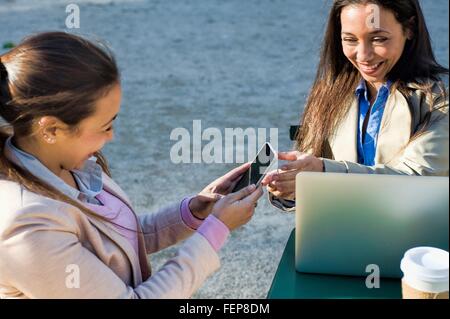 Junge Erwachsene weibliche Zwillinge mit Laptop und Smartphone im Straßencafé Stockfoto