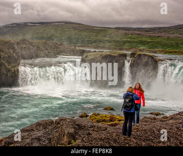 1. August 2015 - BáRðArdalur District, North Central Island, Island - fotografiert eine junge Frau Tourist anderen am hufeisenförmigen doppelten Wasserfall des berühmten Goðafoss aus der Westbank. Einer der spektakulärsten und schönsten Wasserfälle in Island, auf dem Fluss Skjálfandafljót, sein Name ist Wasserfall der Götter aus der Legende des dann Lawspeaker Porgeir wirft seinen nordischen Gott Statuen in den Wasserfall in einem symbolischen Akt der Bekehrung des Island zum Christentum im Jahr 1000. Der Tourismus ist ein wachsender Sektor der Wirtschaft geworden und Island ist ein beliebtes Touristenziel geworden. Stockfoto