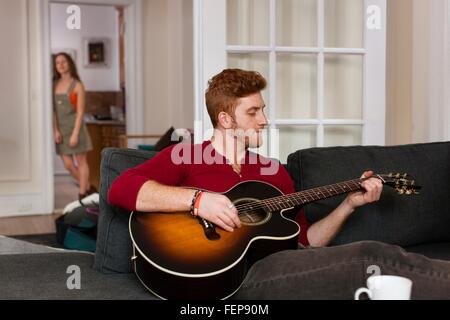 Junger Mann sitzen Sofa Gitarre spielen Stockfoto
