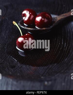 Frische schwarze Kirschen auf Holzlöffel in Schüssel mit Wasser Stockfoto