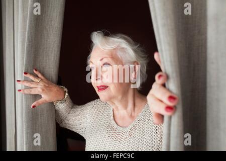 Ältere Frau, die Vorhänge öffnen Stockfoto