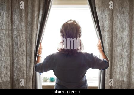 Ältere Frau öffnen Vorhänge, Rückansicht Stockfoto