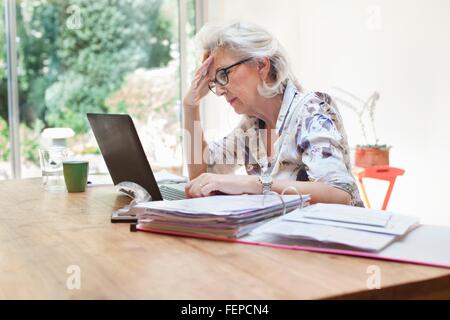 Ältere Frau sitzt am Tisch, mit Laptop, besorgt Ausdruck Stockfoto