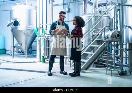 Gesamtansicht der Länge der Kolleginnen und Kollegen im Brauerei-Holding-Zwischenablage, stehend im Gespräch Stockfoto