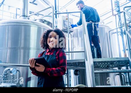 Mitte erwachsenen Frau in Brauerei trägt Schürze mit digital-Tablette Blick auf die Kamera zu Lächeln Stockfoto