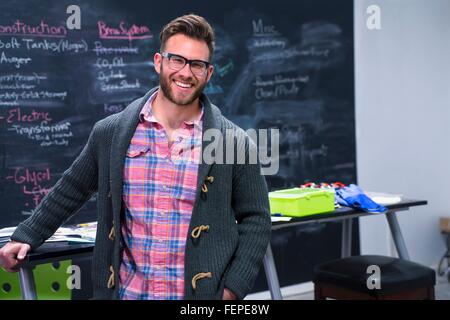 Junger Mann Arbeitsplatz tragen Strickjacke und Gläser, Blick auf die Kamera zu Lächeln Stockfoto