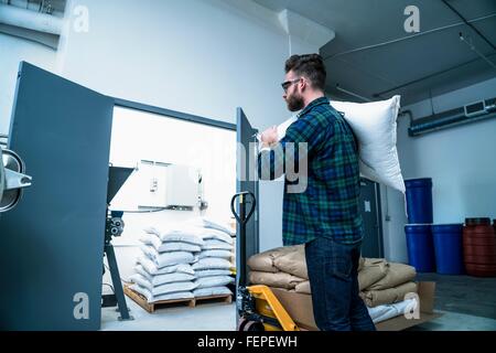 Seitenansicht des Jünglings im Warehouse Sackleinen Sack auf der Schulter tragen Stockfoto