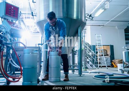 Junger Mann in der Brauerei von konischer Gärtank Kanister Schlauch zuweisen Stockfoto